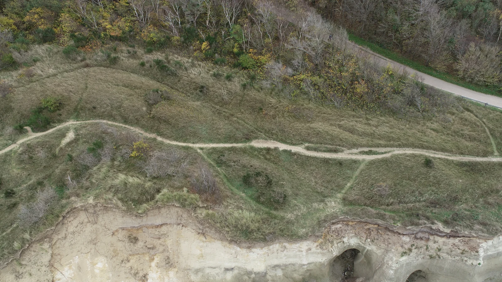 A drone photograph of a coastal site with footpaths and a cliff face.